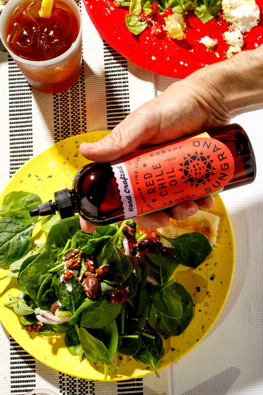 A hand holding a bottle of Sungrano over a spinach salad